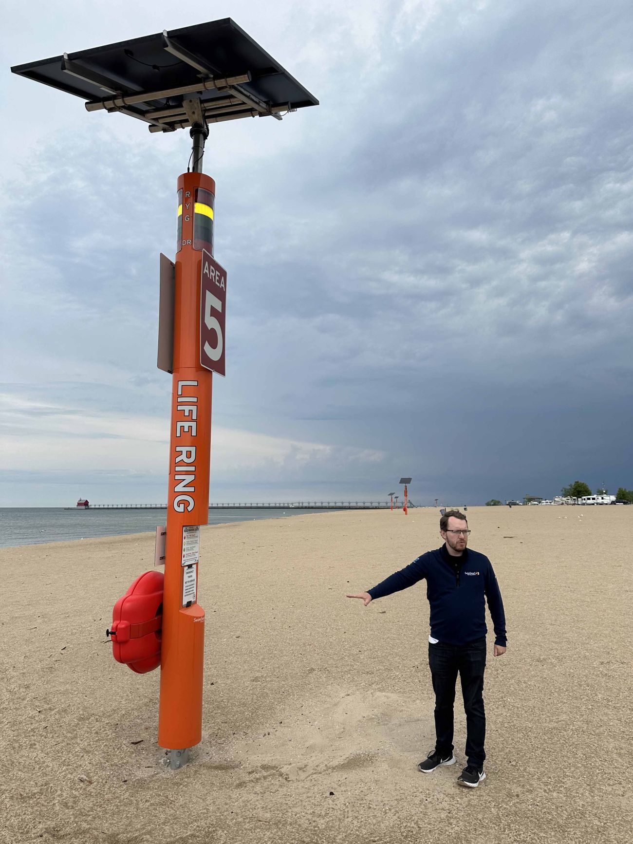 Man on the beach. Next to him is a huge orange pole.