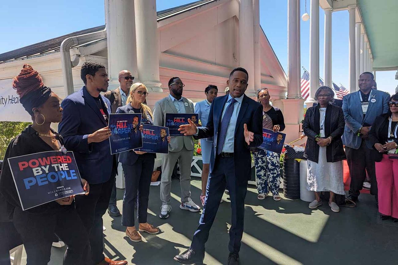 Hill Harper is wearing a blue shirt. He surrounded by supporters