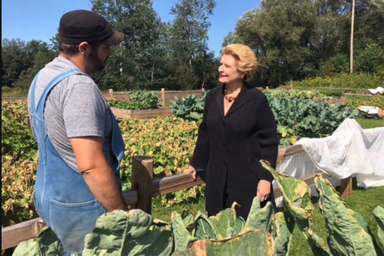 Debbie Stabenow is standing in a farm field. She is talking to a man in overalls