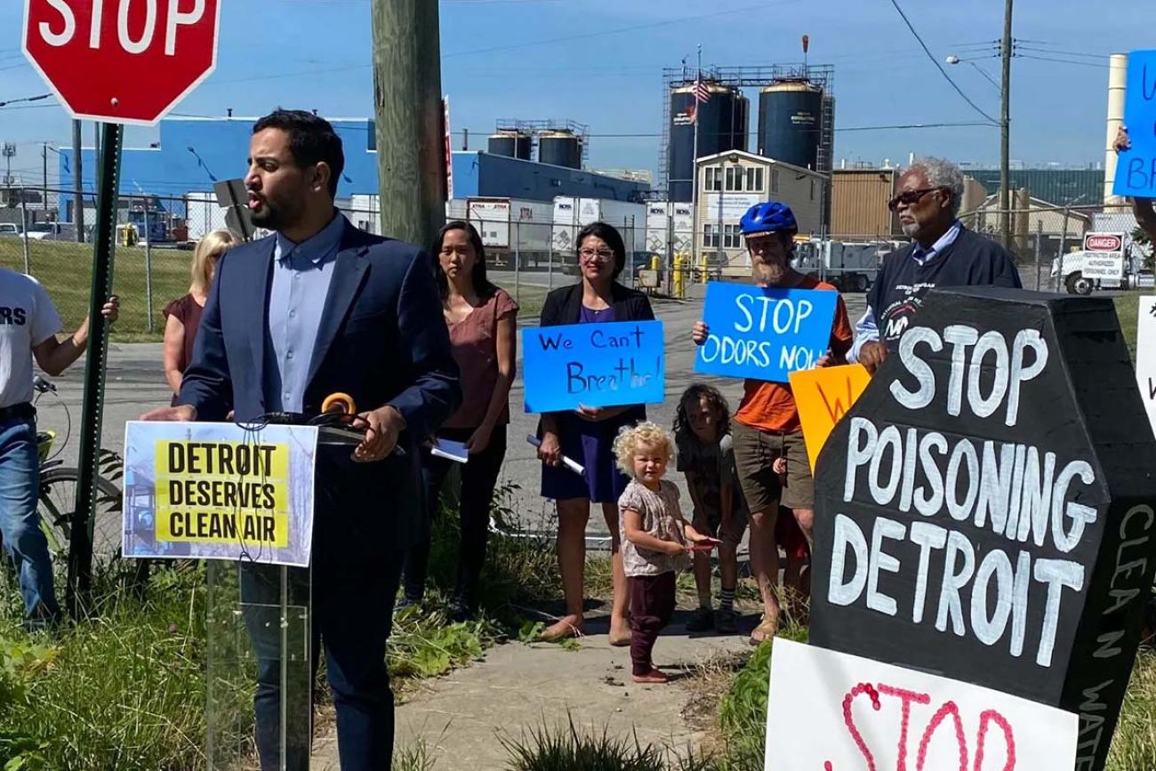 State Rep. Abraham Aiyash (D-Hamtramck) speaks at a protest at the US Ecology hazardous waste facility in Detroit. People are standing behind. They are on a street corner