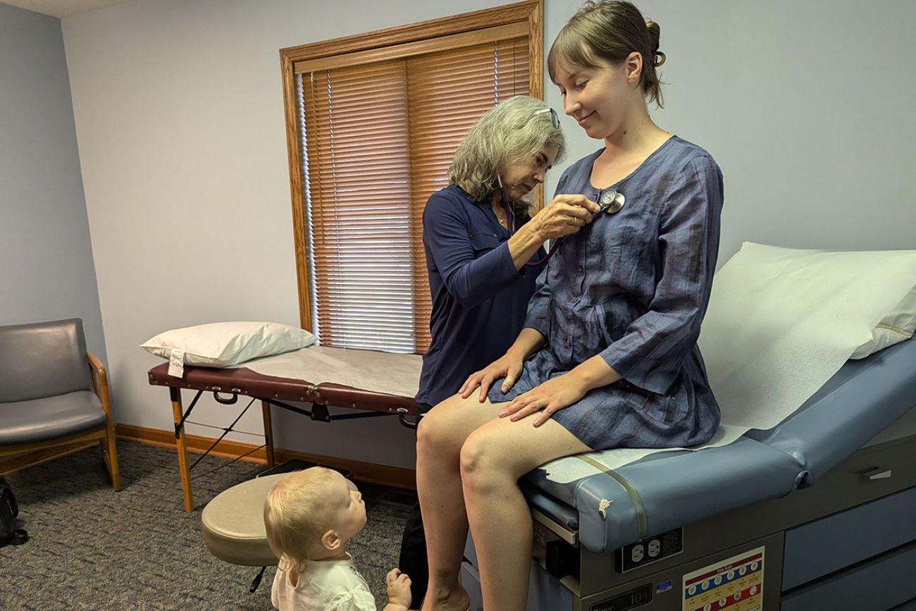 Emily Chumbler sits down while Dr. Cheryl Canfield listens to her chest. A toddler locks on her mom during the exam