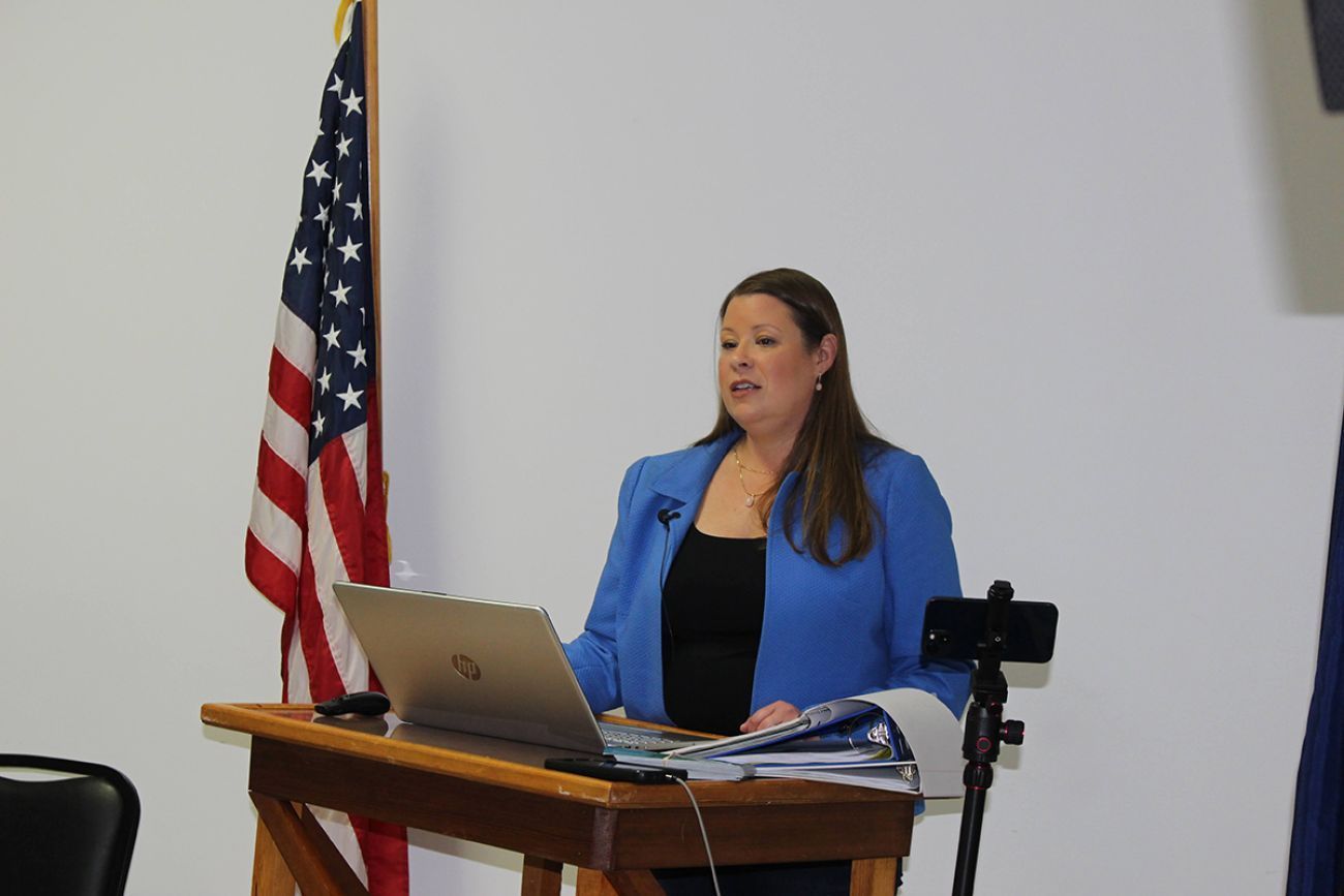 Stefanie Lambert at a podium. She is wearing a blue blazer