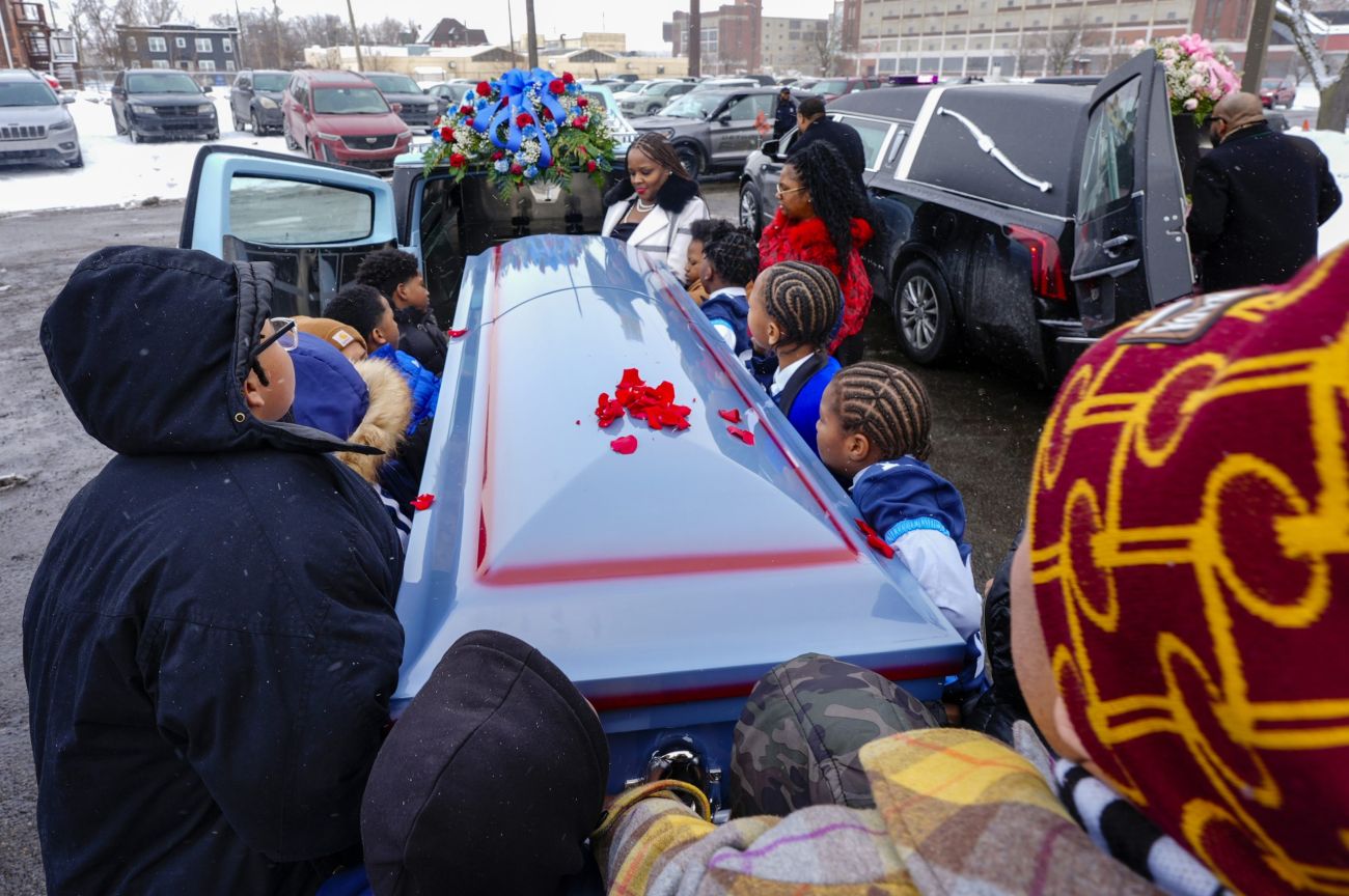 Many people are carrying a casket and putting it in a hearse.