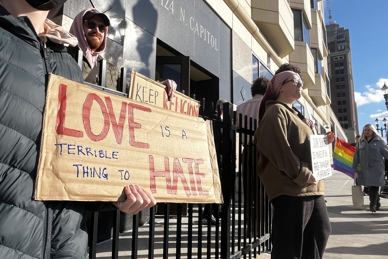 Someone holding a sign that says "Love is a terrible thing to hate,"