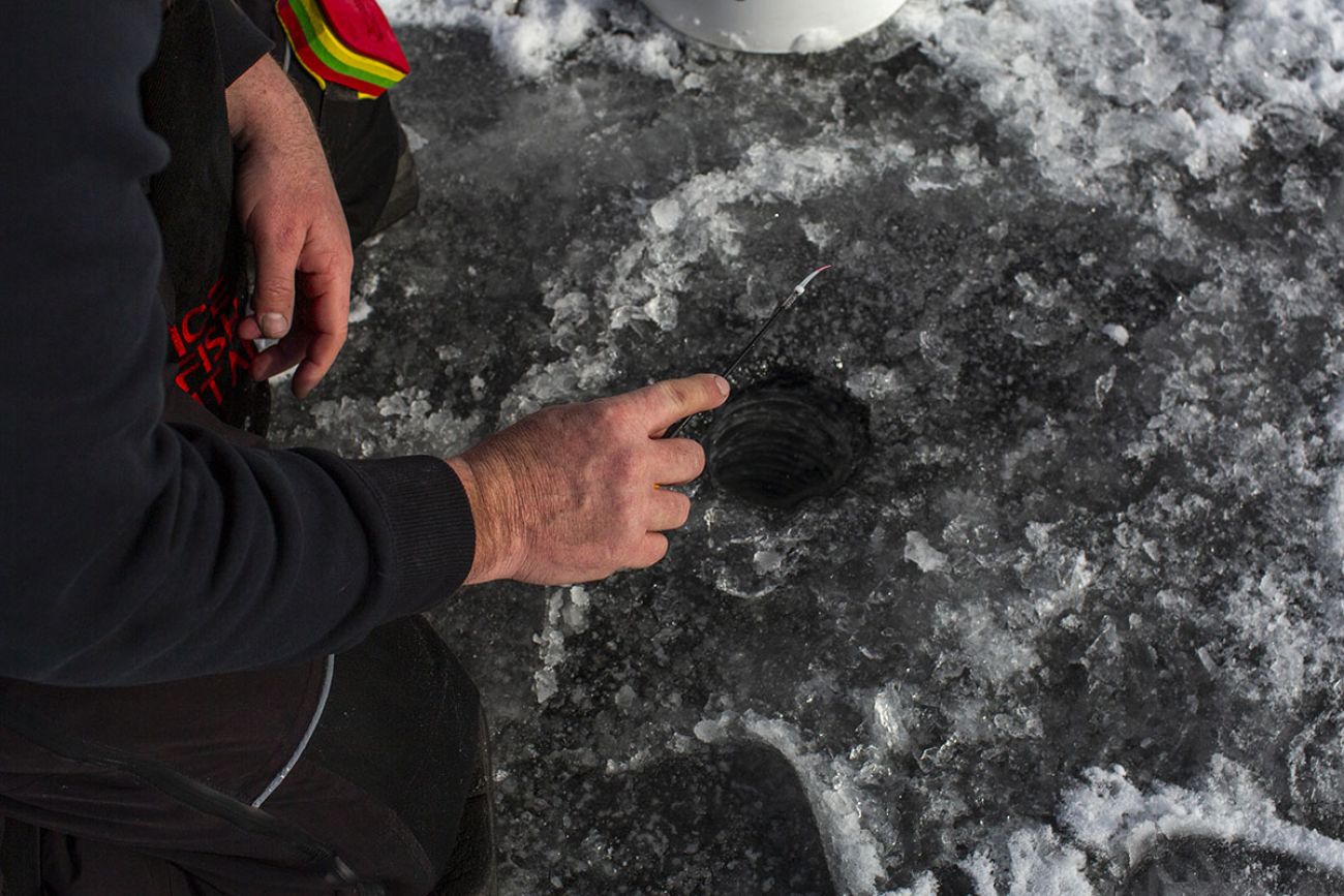 Joe Martinez kneeling by a hole in the ice.