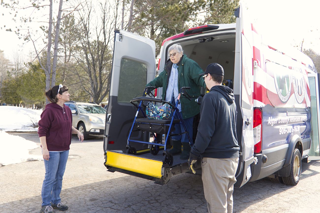 A woman in a wheelchair being lowered from the back of a van.