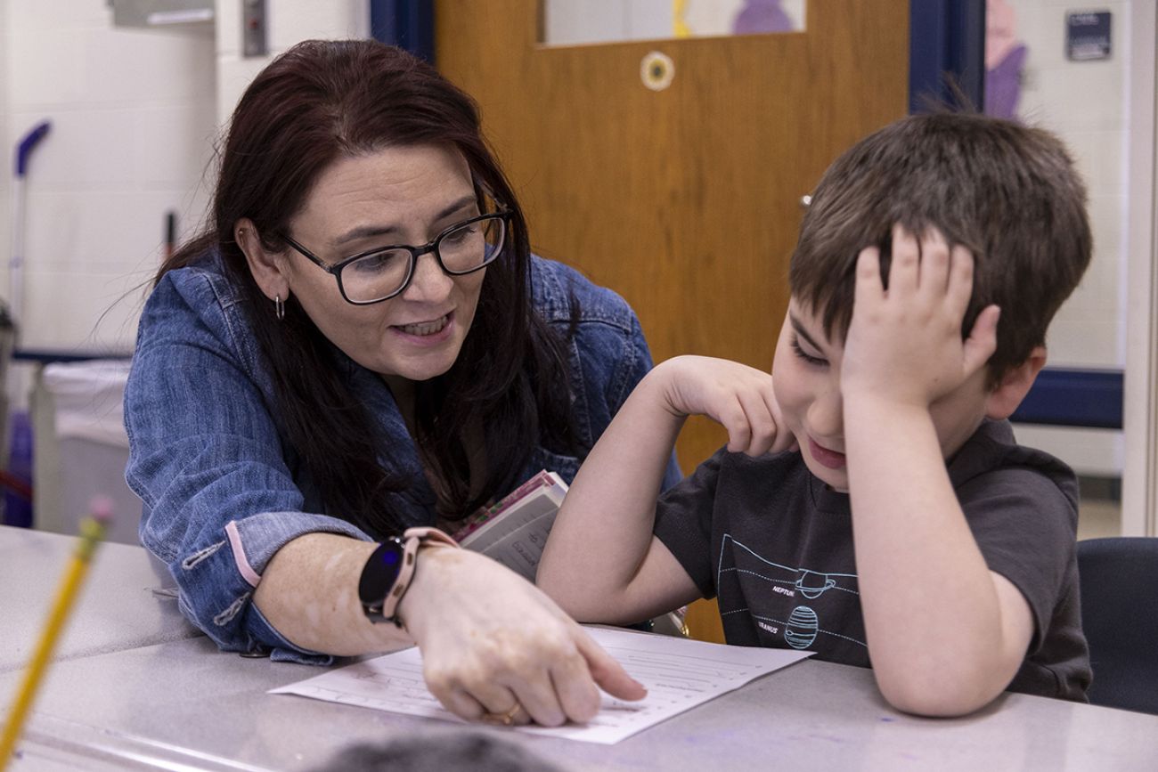 Literacy coach Cindy Stacy looks over a paper with a boy sitting at his desk.