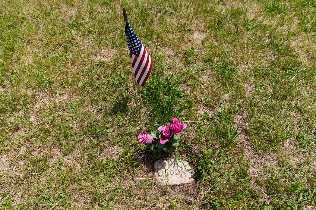 A small headstone. There are pink flowers and a small American flag close by.