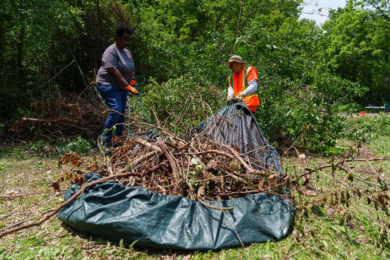 Two people pull a green tarp carrying branches at the Woodlawn Cemetery in Ypsilanti, Michigan.