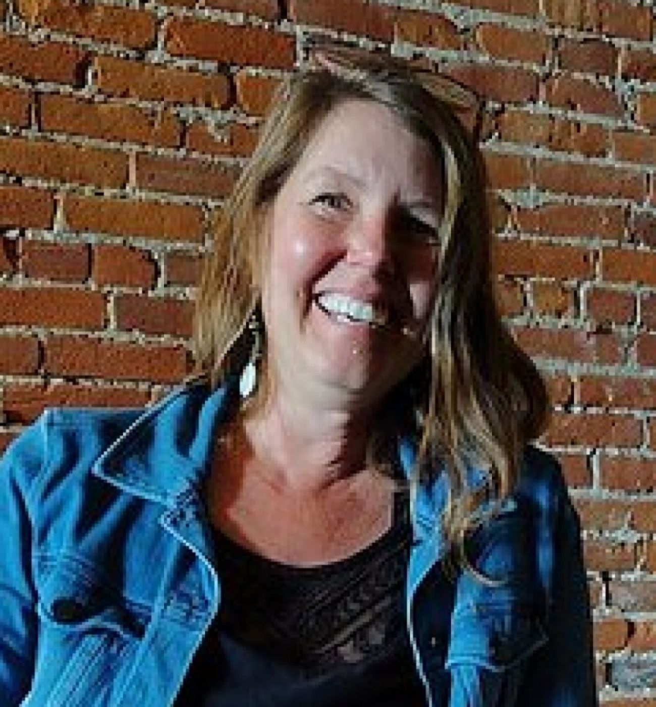 A woman smiles with a brick wall behind her