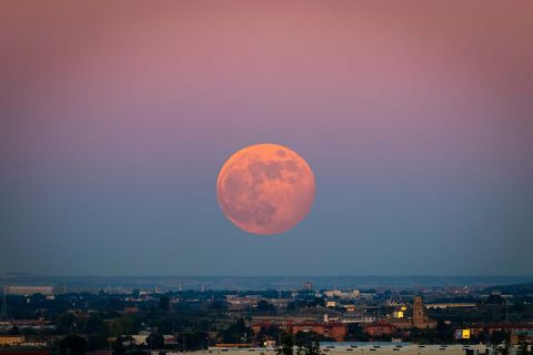 The strawberry Supermoon at sunset gradient from blue to pink on the city skyline in June 2020 in Spain.