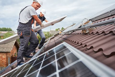 Two men install solar panels on a roof. 