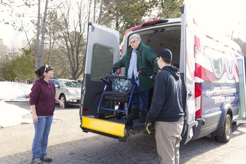 A woman in a wheelchair being lowered from the back of a van.
