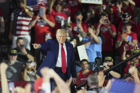 President Donald Trump walks on stage. People are behind him.