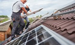 Two men install solar panels on a roof. 