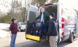 A woman in a wheelchair being lowered from the back of a van.