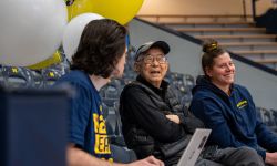 Sandy Vong sits in the bleachers, talking to two players.